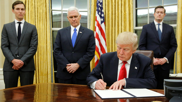 U.S. President Donald Trump, flanked by Senior Advisor Jared Kushner (standing, L-R), Vice President Mike Pence and Staff Secretary Rob Porter welcomes reporters into the Oval Office for him to sign his first executive orders at the White House in Washington, U.S. January 20, 2017. REUTERS/Jonathan Ernst
