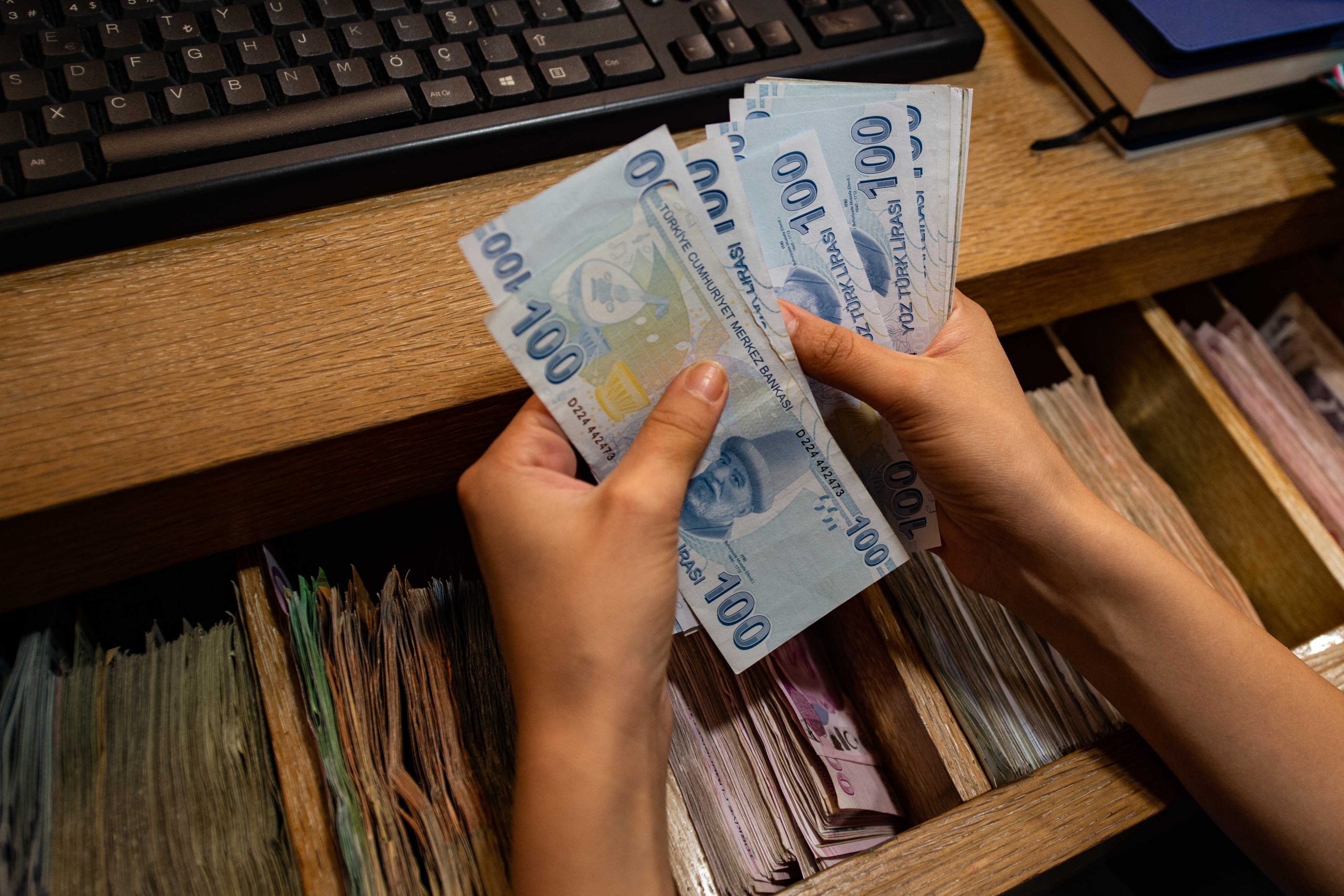 A currency exchange office worker counts Turkish Lira banknotes in front of the electronic panel displaying currency exchange rates at an exchange office in Istanbul, on August 6, 2020 as Turkey's lira set a new record low against the US dollar. - The lira on August 6 was trading at 7.28 against the greenback around 1030 GMT, suffering a loss of more than 3 percent since the start of the day -- the lowest since May when it reached a then-record low of 7.24. The currency also recorded its lowest level against the euro, trading near 8.60 against the European currency at 1030 GMT. (Photo by Yasin AKGUL / AFP)